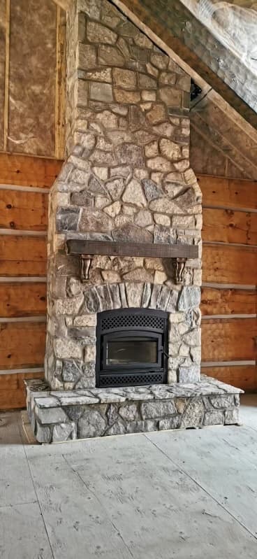 Custom floor-to-ceiling stone fireplace with wooden mantel and insert